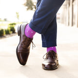 Person wearing brown dress shoes and purple socks with multi-colored polka dots on a blurred outdoor background.