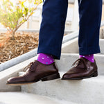 Person wearing navy trousers, brown shoes and purple socks with white polka dots on a concrete stairs.