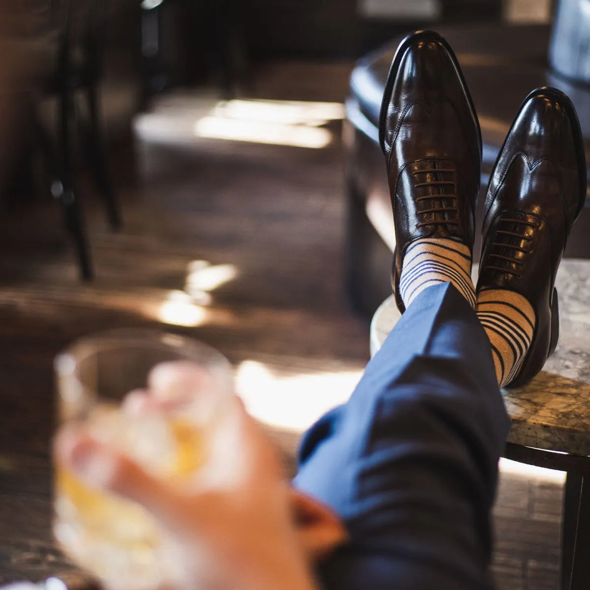 Man wearing tan, navy blue, and white striped dress socks and dark brown dress shoes