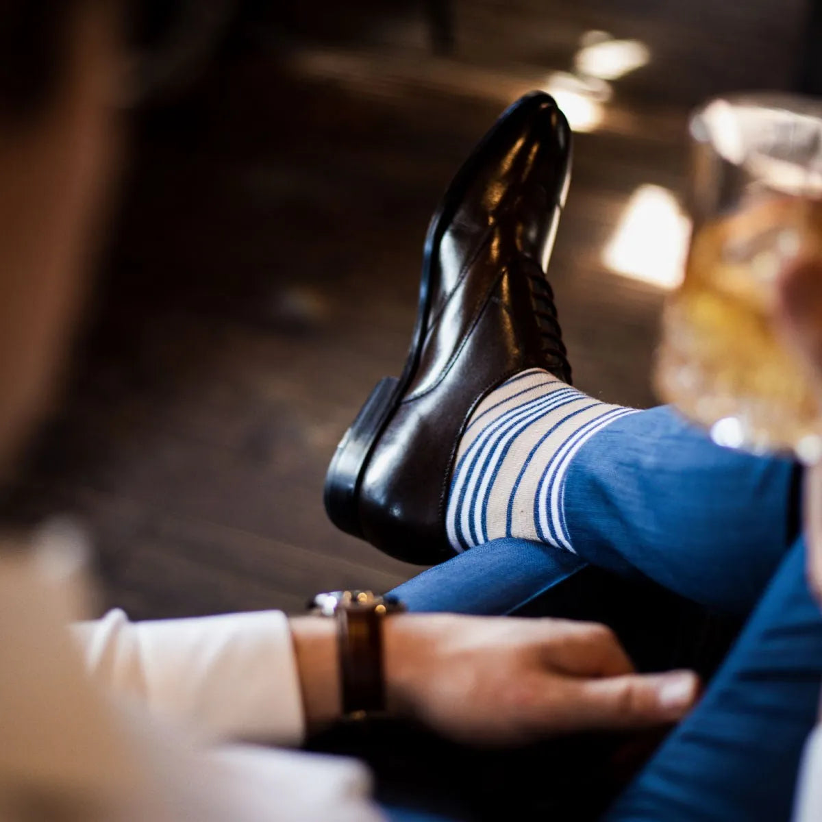 A man wearing tan, navy blue, and white striped dress socks and dark brown dress shoes
