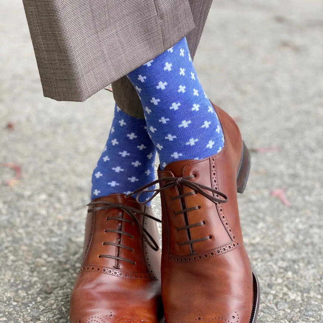 Man standing with feet crossed wearing heathered blue socks with white hatches and dress shoes