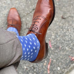 Man sitting with legs crossed wearing heathered blue socks with white hatches and dress shoes