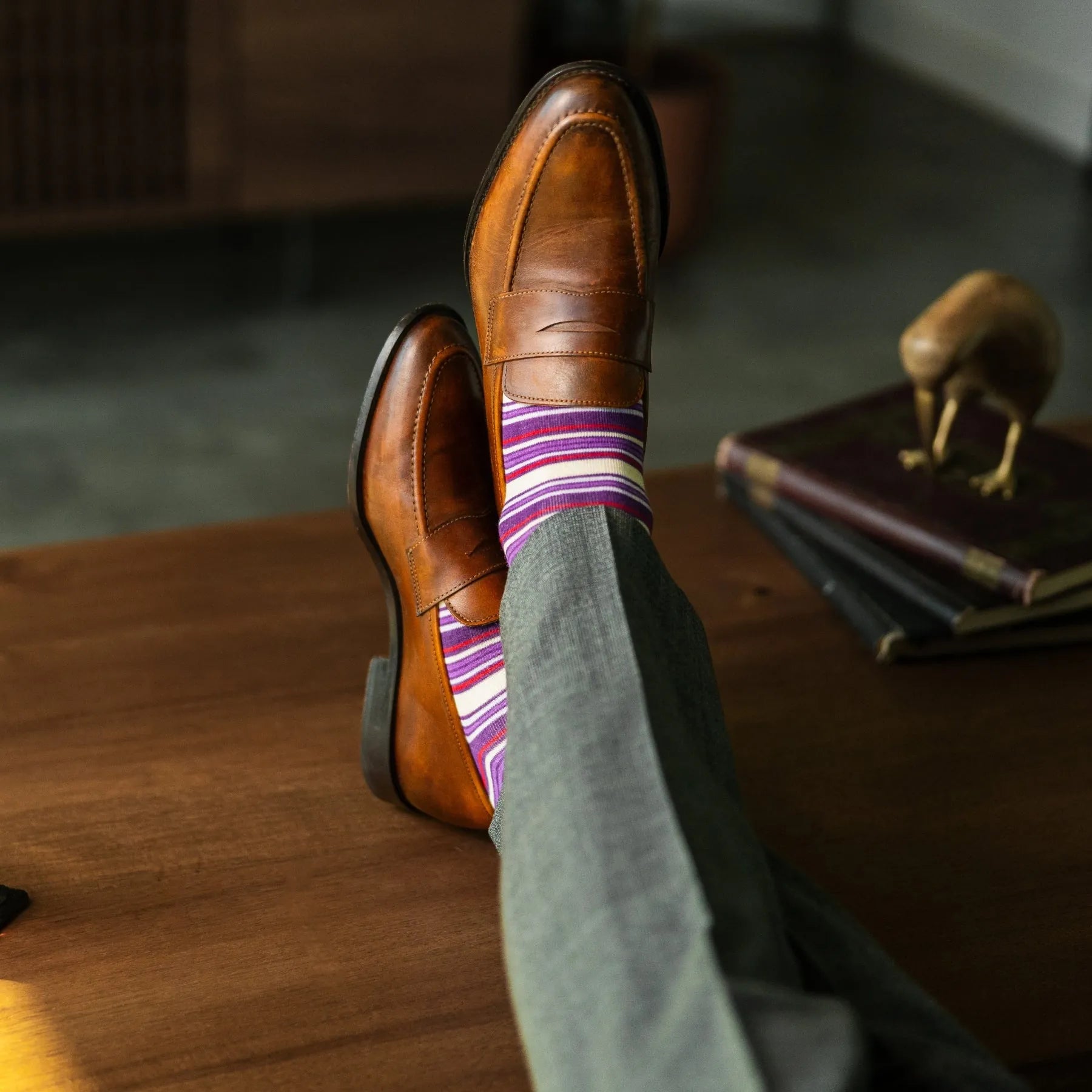 Person wearing purple stripe men's dress socks with brown shoes and gray pants on a checkered floor.
