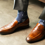  A Prussian blue sock with a crisp white nested diamond pattern, worn with brown leather loafers and grey trousers.