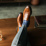  A Prussian blue sock with a crisp white nested diamond pattern, worn with brown leather loafers and grey trousers.