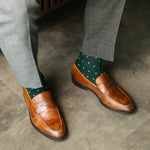 A deep green men's dress sock with clean white accents, worn with grey trousers and brown loafers. 
