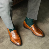 A deep green men's dress sock with clean white accents, worn with grey trousers and brown loafers. 