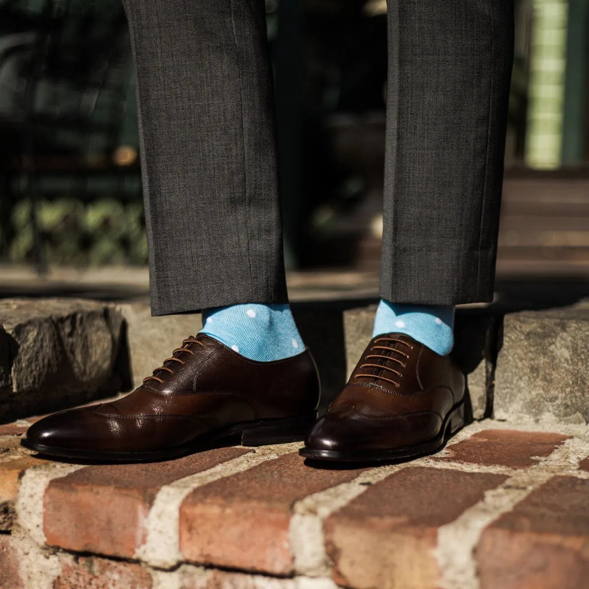 Man wearing charcoal grey slacks, baby blue and white polka dot socks, and brown dress shoes