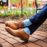 Man sitting with legs crossed wearing navy blue pants, baby blue and white polka dot socks, and tan shoes.