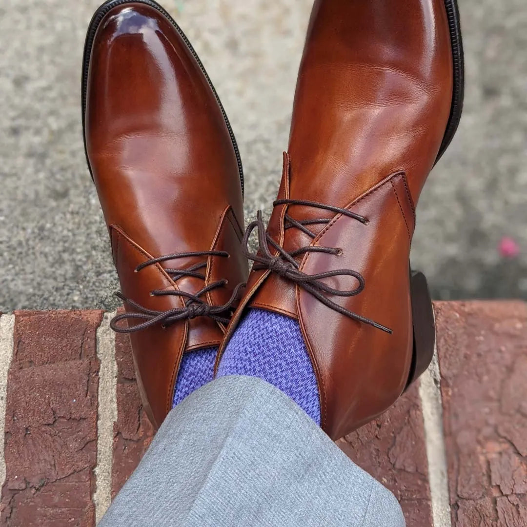 Man sitting with legs crossed wearing purple socks and brown shoes