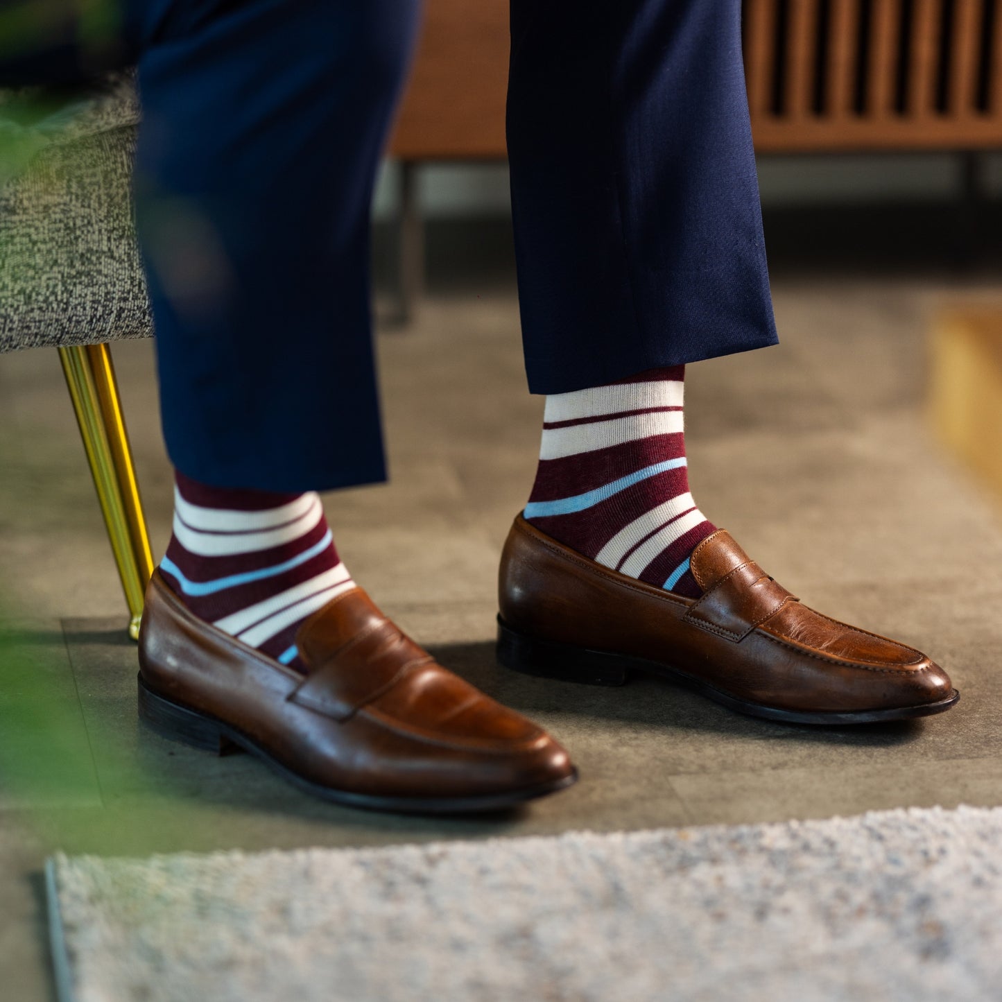 A cranberry red men's dress sock with cream and light blue stripes.