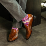 Person wearing purple stripe men's dress socks with brown shoes and gray pants on a checkered floor.