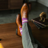 Person wearing purple stripe men's dress socks with brown shoes and gray pants on a checkered floor.