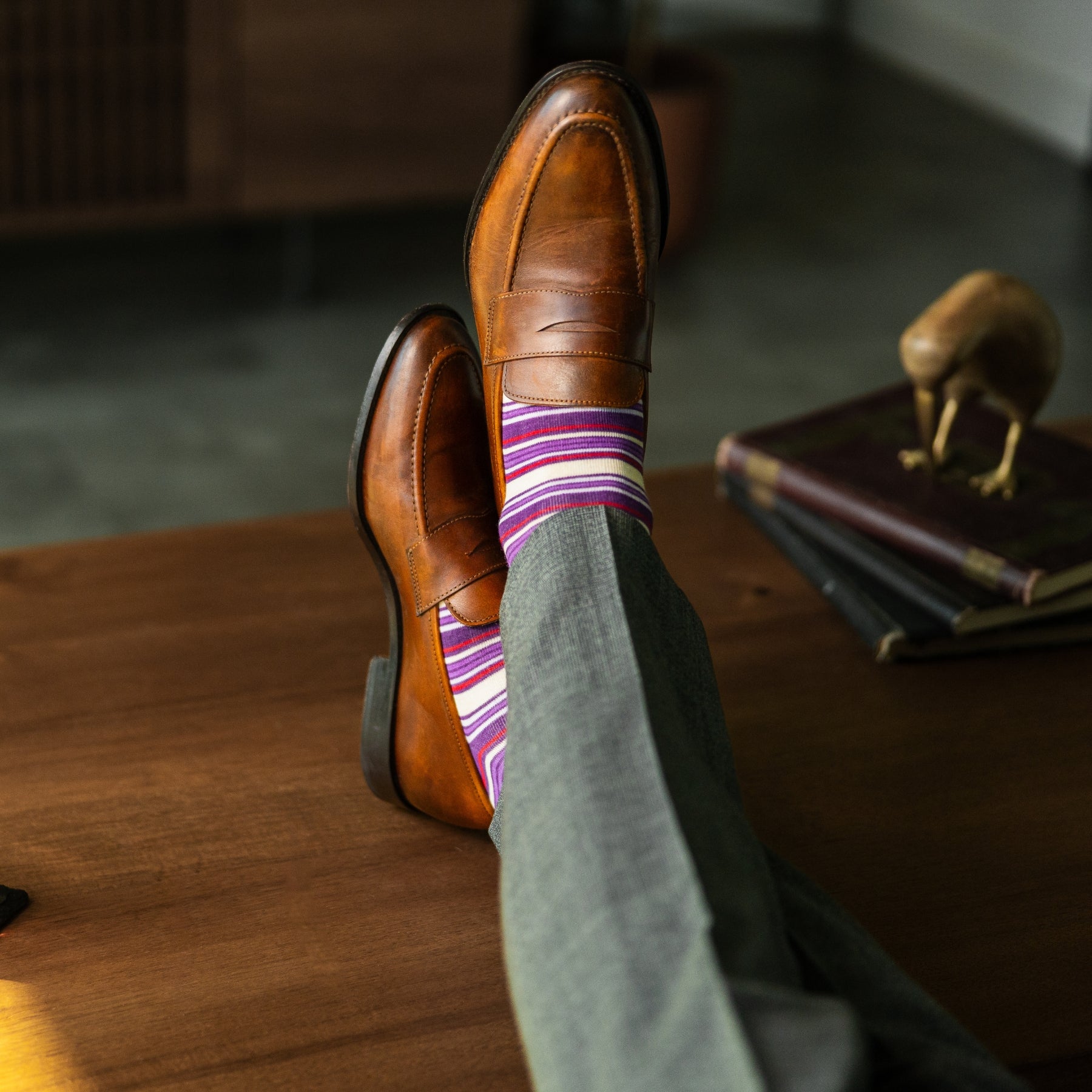 Person wearing purple stripe men's dress socks with brown shoes and gray pants on a checkered floor.