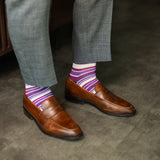 Person wearing purple stripe men's dress socks with brown shoes and gray pants on a checkered floor.