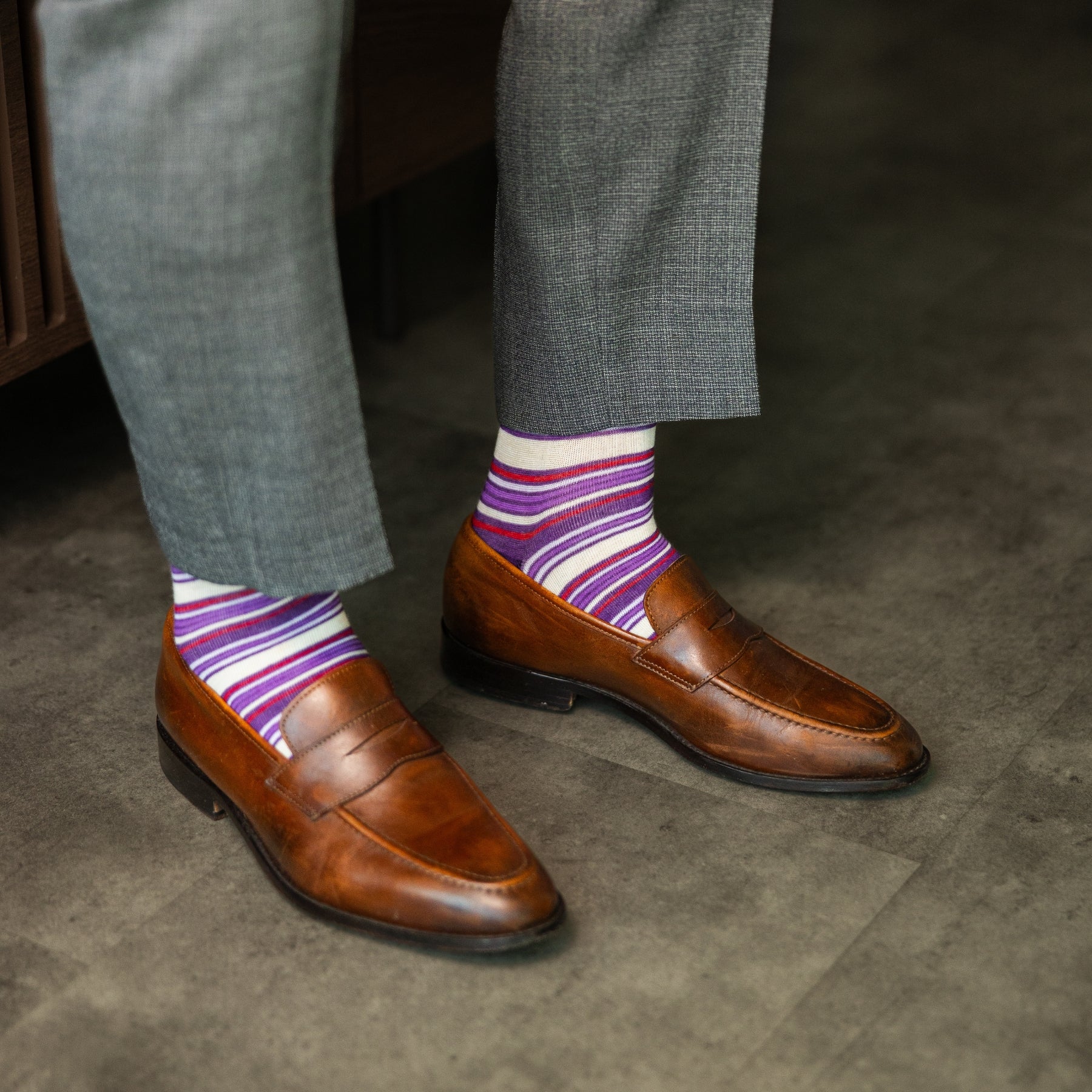 Person wearing purple stripe men's dress socks with brown shoes and gray pants on a checkered floor.