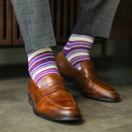 Person wearing purple stripe men's dress socks with brown shoes and gray pants on a checkered floor.