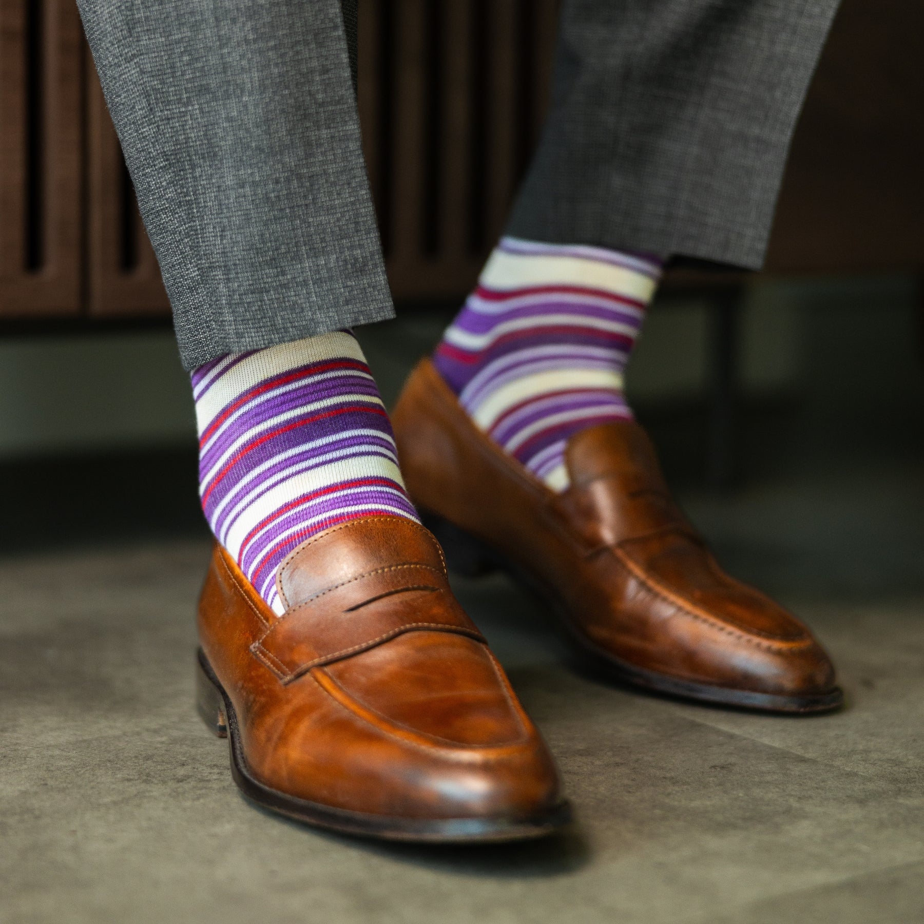 Person wearing purple stripe men's dress socks with brown shoes and gray pants on a checkered floor.