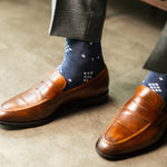  A Prussian blue sock with a crisp white nested diamond pattern, worn with brown leather loafers and grey trousers.