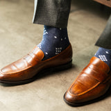  A Prussian blue sock with a crisp white nested diamond pattern, worn with brown leather loafers and grey trousers.
