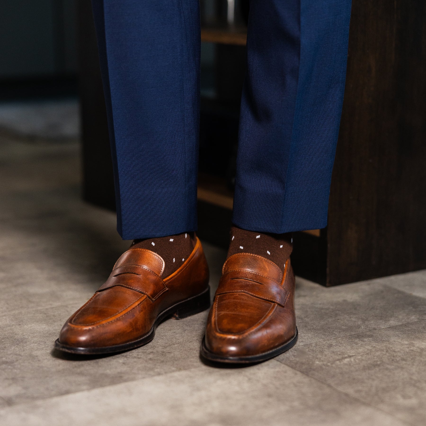 Rich chocolate brown men's dress socks with clean white accents, paired with navy trousers and brown leather loafers