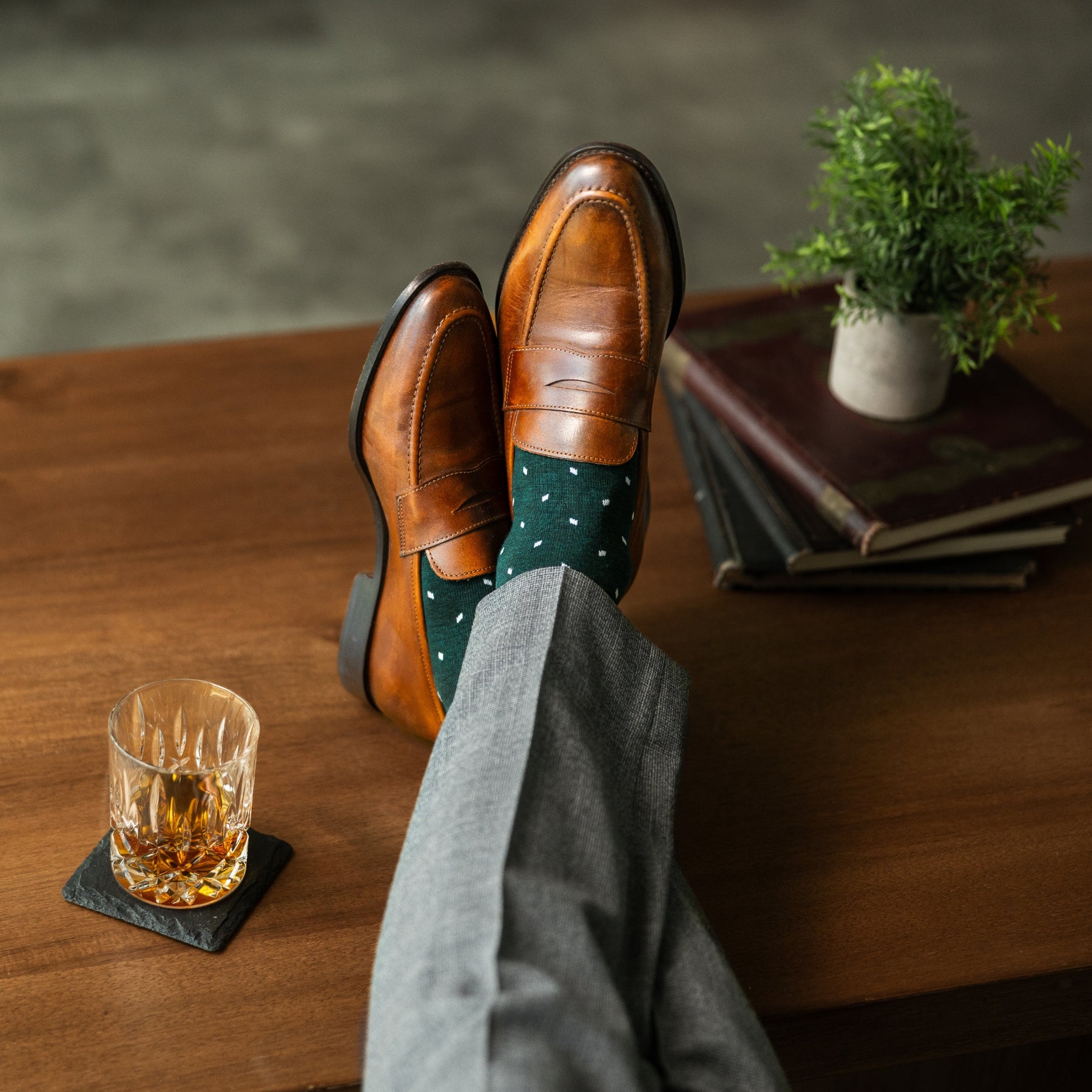 A deep green men's dress sock with clean white accents, worn with grey trousers and brown loafers. 