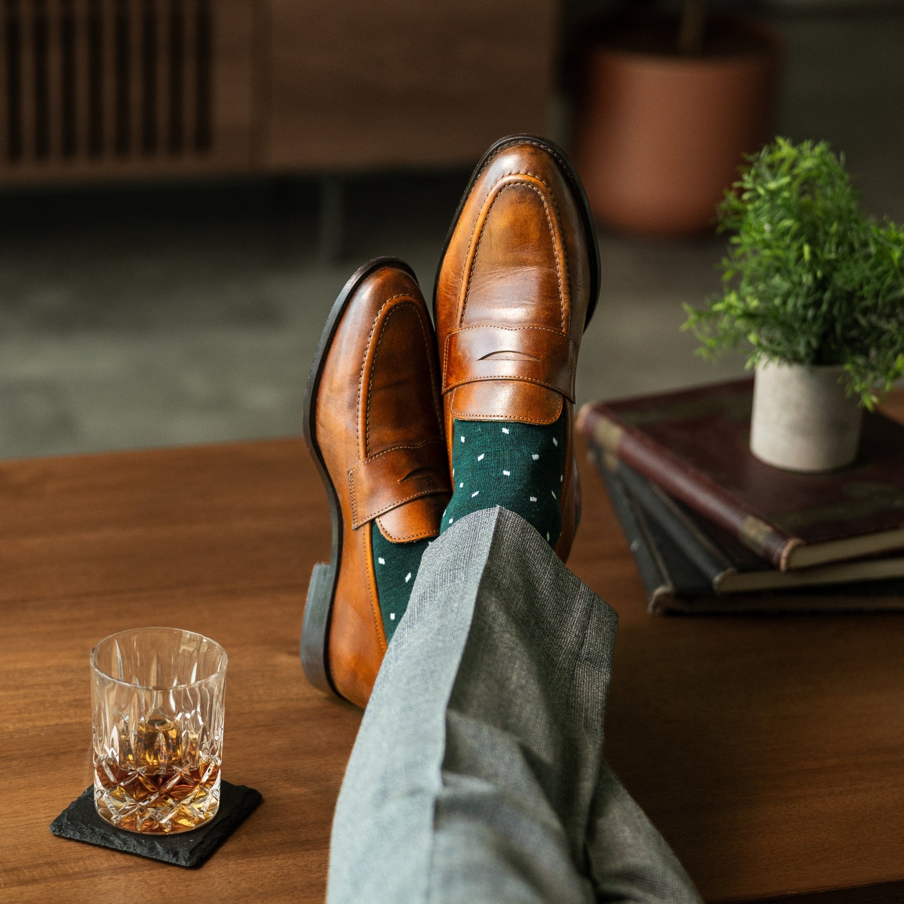 A deep green men's dress sock with clean white accents, worn with grey trousers and brown loafers. 