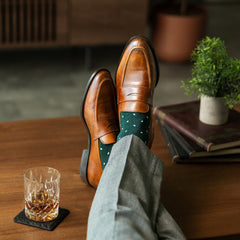 A deep green men's dress sock with clean white accents, worn with grey trousers and brown loafers. 