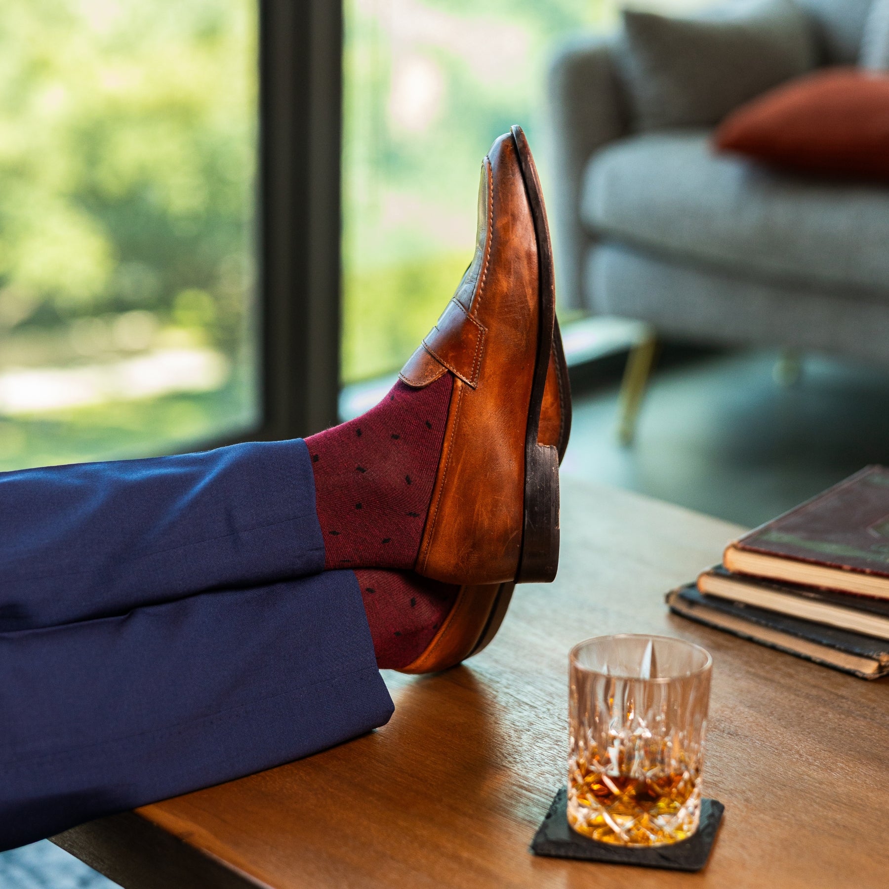 Person wearing brown leather shoes and red patterned socks with a glass of whiskey on a coaster.
