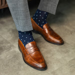 Brown loafers and navy socks with white polka dots on a concrete floor.
