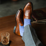 Brown leather shoes with blue patterned socks on a wooden table with a glass of whiskey.