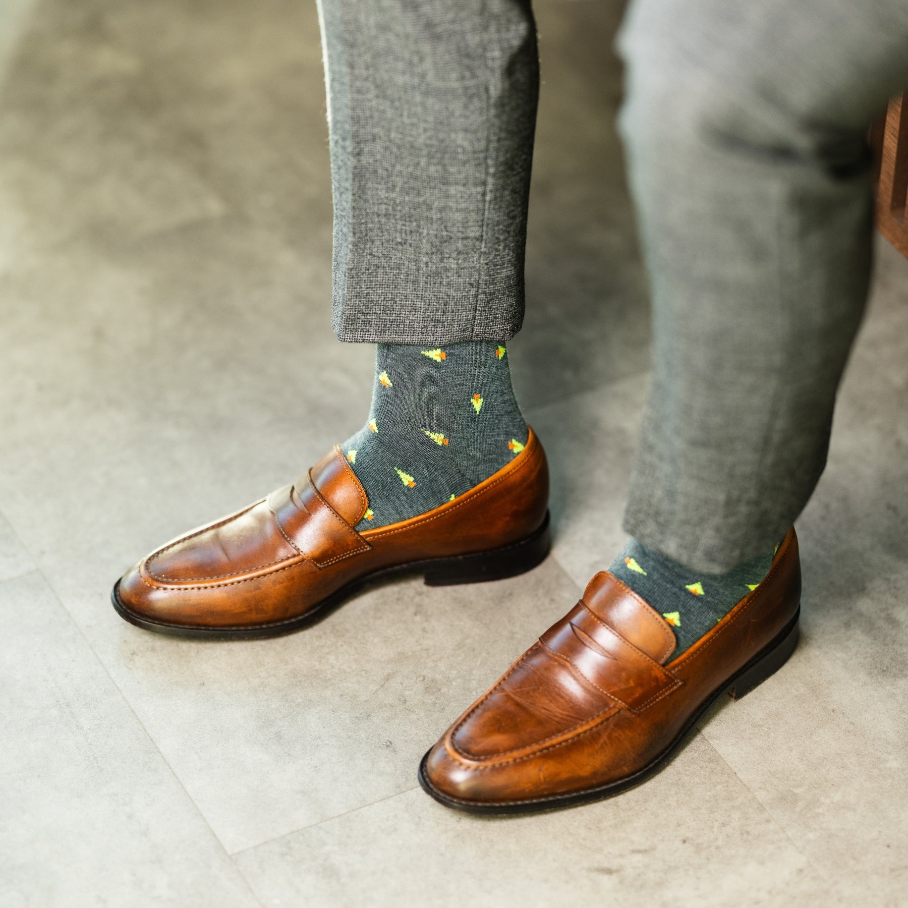 A charcoal-green sock with warm orange and green pine tree motifs, designed to add a subtle seasonal touch with refined, modern appeal.