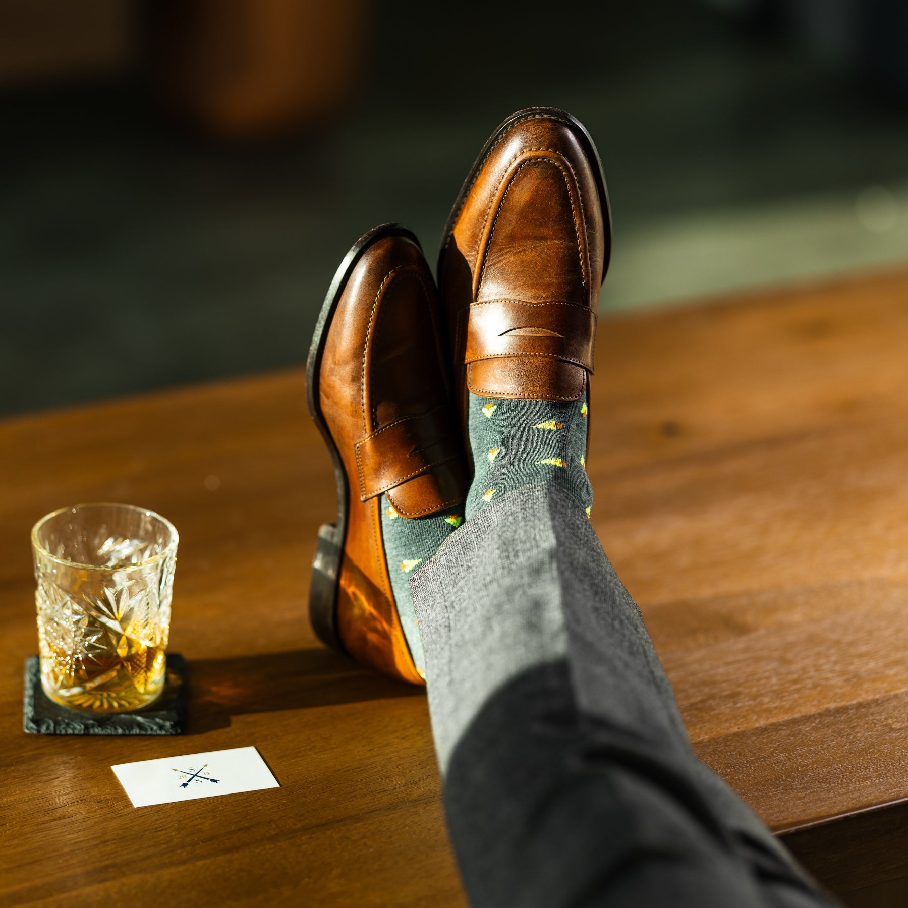 A charcoal-green sock with warm orange and green pine tree motifs, designed to add a subtle seasonal touch with refined, modern appeal.