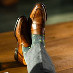 A charcoal-green sock with warm orange and green pine tree motifs, designed to add a subtle seasonal touch with refined, modern appeal.