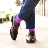 Person wearing brown dress shoes and purple socks with multi-colored polka dots on a blurred outdoor background.