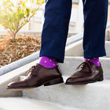 Person wearing navy trousers, brown shoes and purple socks with white polka dots on a concrete stairs.