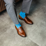 Person wearing brown shoes and blue socks with a pattern on a concrete floor.