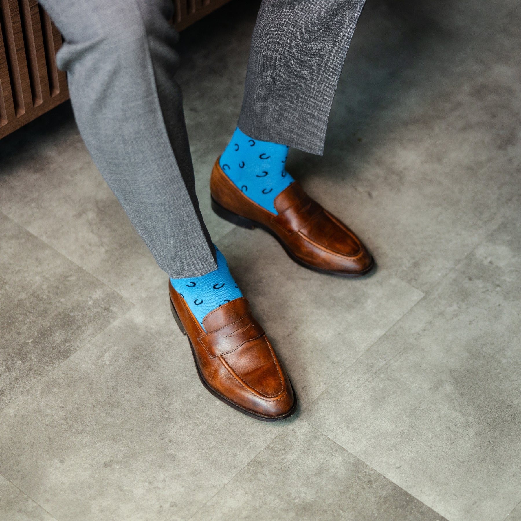 Person wearing brown shoes and blue socks with a pattern on a concrete floor.