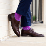 Brown dress shoes and purple polka dot socks against a neutral background