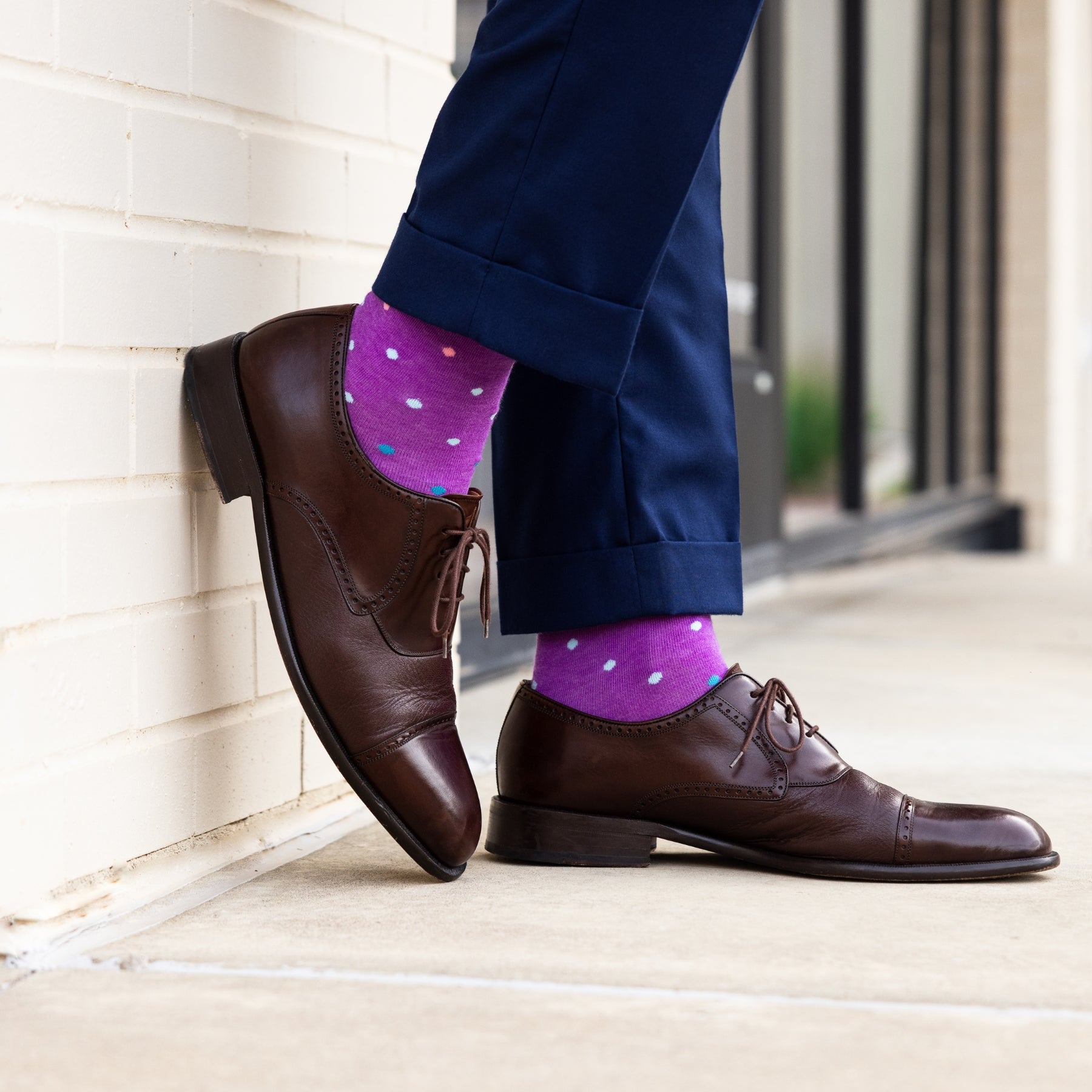 Brown dress shoes and purple polka dot socks against a neutral background