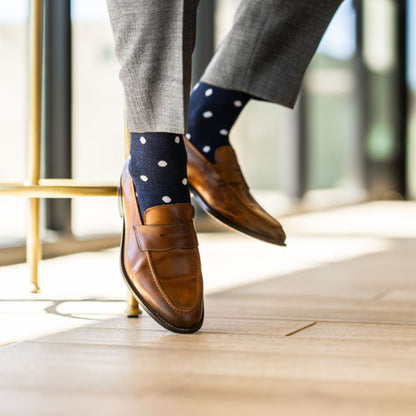 Man wearing grey pants, navy blue socks with white polka dots, and brown dress shoes.
