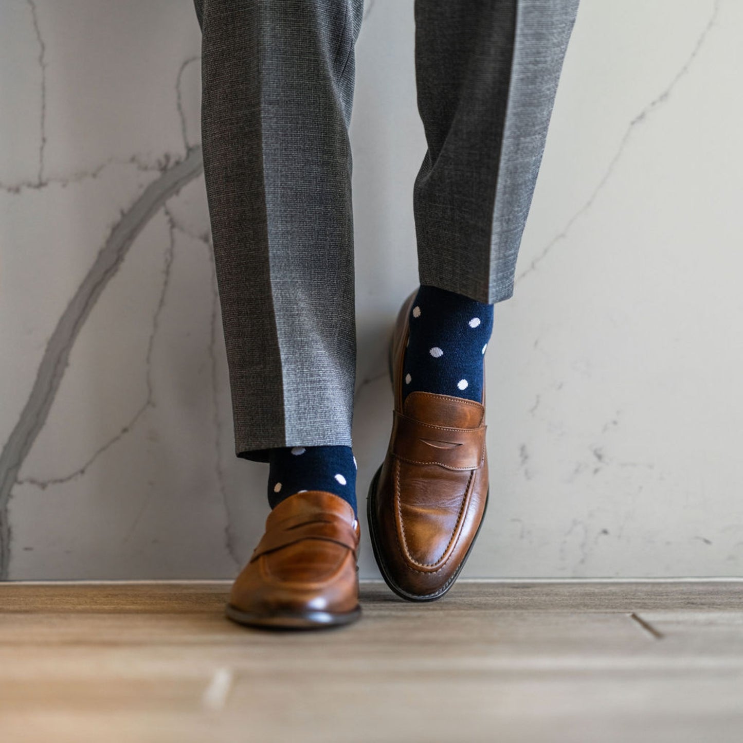 Man wearing grey pants, navy blue socks with white polka dots, and brown dress shoes.