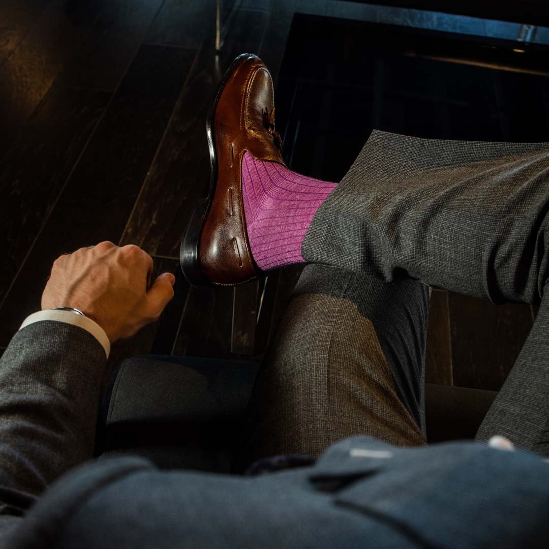 Man sitting wearing fuchsia, solid, ribbed men's dress socks with brown shoes