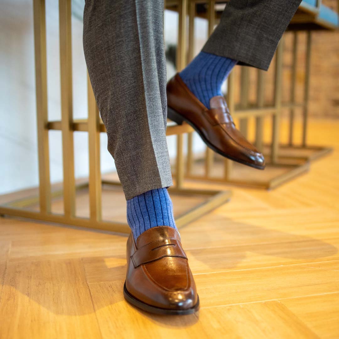 Man sitting wearing solid, blue, and navy blue ribbed men's dress socks and brown shoes.