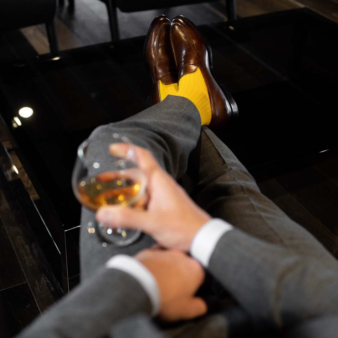 Man sitting, taking wine wearing honeycomb, solid, ribbed men's dress socks with brown shoes.