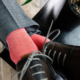 A man wearing A coral and salmon men's dress sock with a micro-chevron pattern with grey slacks and brown shoes
