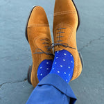 Man sitting with legs crossed wearing sapphire blue, sand and white micro-square socks with brown shoes