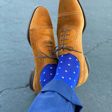 Man sitting with legs crossed wearing sapphire blue, sand and white micro-square socks with brown shoes