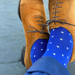 Man sitting with legs crossed wearing sapphire blue, sand and white micro-square socks with brown shoes