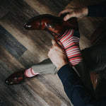 Man wearing coral, grey and white striped socks and dress shoes